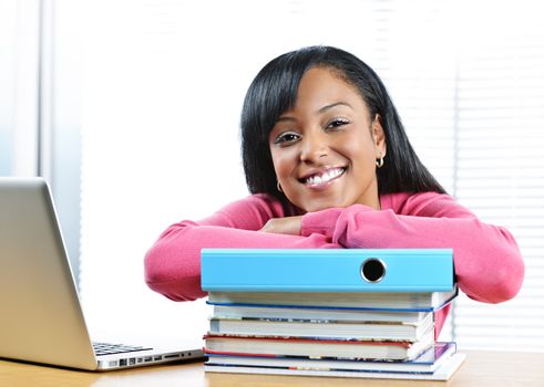 Smiling young black female student with textbooks at desk