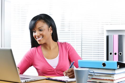 Smiling young black female student with computer and textbooks at desk