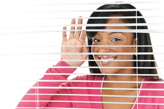 Happy young black woman looking through horizontal venetian blinds
