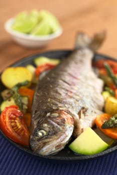 Baked trout and vegetables on metal plate with lime in the back (Selective Focus, Focus on the eye of the fish)