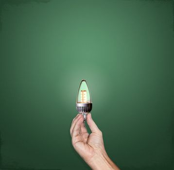 Hand holding a bright LED lightbulb in front of a green chalkboard with plenty of copy space