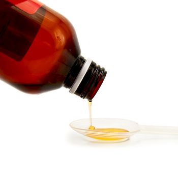 Yellow syrup poured from a brown bottle in a plastic spoon isolated on white background