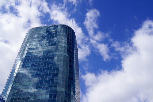 Blue skyscraper in white clouds, wich are reflected in its surface
