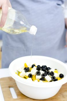 Greek salad preperation: oil pours on greek salad