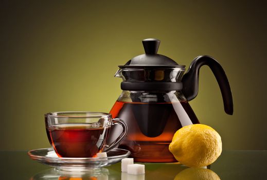 glassy teacup and teapot with tea and lemon