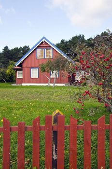 Colorful homestead house with a large yard and garden. Tree with red fruit.