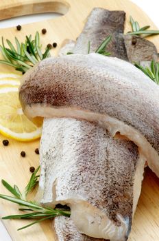 Heap of Raw Fish Hake Fillets with Lemon, Black Peppercorn and Rosemary closeup on Cutting Board