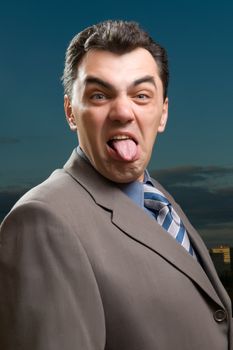 man in a suit against the evening sky shows tongue