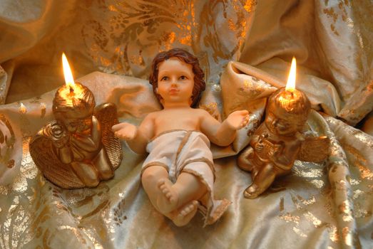 Christmas card, baby Jesus and two lighted candles on a cloth of gold