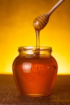 Honey jar with dipper and flowing honey, canvas background 