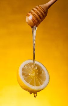 Honey flowing on lemon over yellow background 