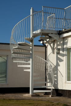 An exterior set of metal spiral stairs leading from a path to a balcony with a blue sky in the background.