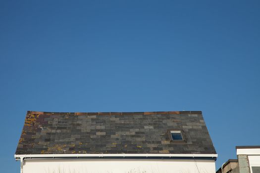 A slate tile roof with sky light, ridge tiles and gutter against a clear blue sky.