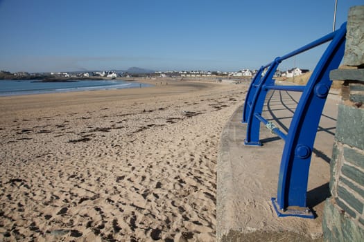 A path and railings curve around the sandy beach of Trearddur bay, Anglesey, Wales, UK.