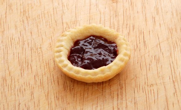 Single tasty jam tart sitting on a wooden table