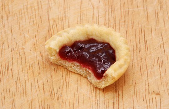 One yummy jam tart with a bite taken from it, on a wooden table
