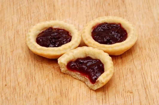 Three yummy jam tarts, one with a bite taken from it, on a wooden table