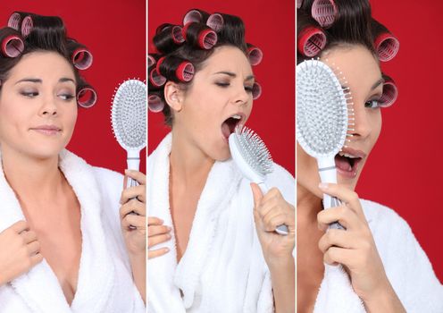 brunette wearing bathrobe with hair curlers holding hairbrush holding against red background