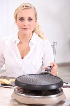 blonde woman in front of a heater preparing melted cheese, potatoes and cold meat (raclette)