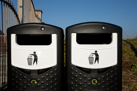 A pair of black and white recycling bins with recycle symbols against a blue sky.