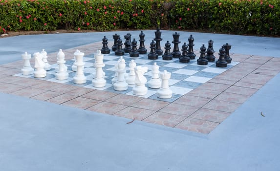 Large white and black pieces in outdoor chess set in flower garden