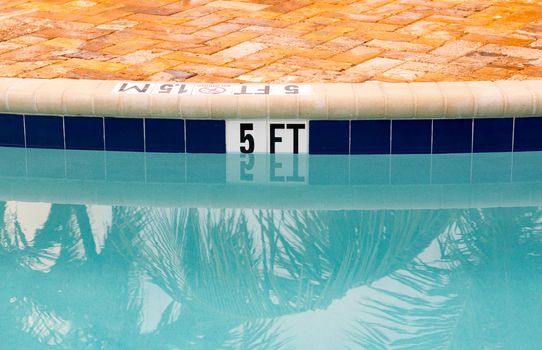 Sign showing 5 ft depth on edge of blue swimming pool with no diving
