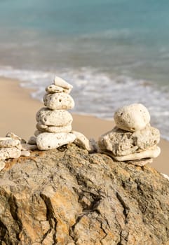 Multiple stacks of pebbles on rock by sea shore with sun lighting the piles