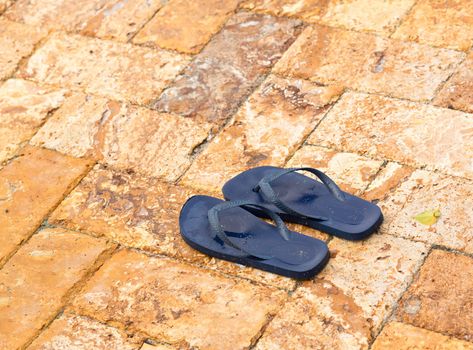 Discarded childs blue flip flops on paved deck by swimming pool with water in indentations