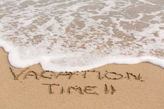 Vacation Time words written into sand on beach by sea in Caribbean