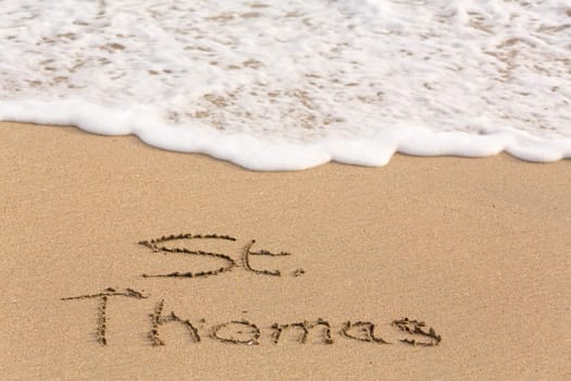 St Thomas words written into sand on beach by sea in Caribbean