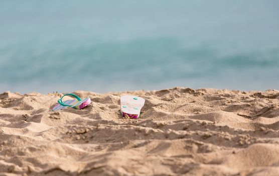 Discarded childs flip flops on sandy beach by turquoise ocean in sun