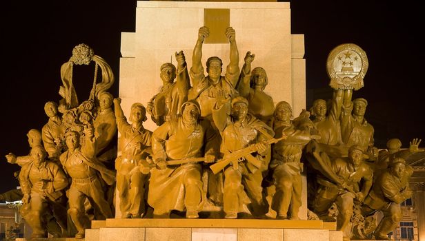 Mao Statue Heroes at the Base of Statue Zhongshan Square Shenyang, Liaoning province, China at Night.  Built in 1969 during the Cultural Revolution.  One hero is holding up copy of a book on the thoughts of Mao Zedong.