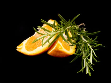 Pieces of orange and fresh rosemary on black background