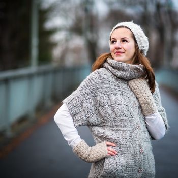 Autumn/winter portrait: young woman dressed in a warm woolen cardigan posing outside in a city park