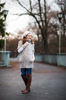 Autumn/winter portrait: young woman dressed in a warm woolen cardigan posing outside in a city park