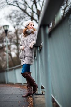 Autumn/winter portrait: young woman dressed in a warm woolen cardigan posing outside in a city park