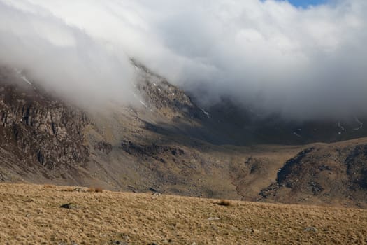 A developing cloud inversion creeps down the rocky mountainside into the valley.