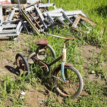 Old abandoned tricycle in grassy field next to junk pile