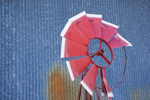 Old red broken windmill against rusted blue corrugated metal building.