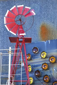 Broken red windmill against rusted blue corrugated metal building covered in taillights.