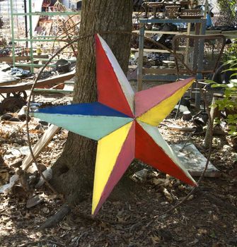 Colorful painted star made of metal leaning against tree.