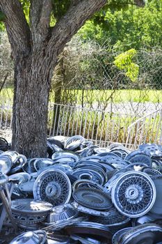 Pile of old hubcaps on the ground next to tree.
