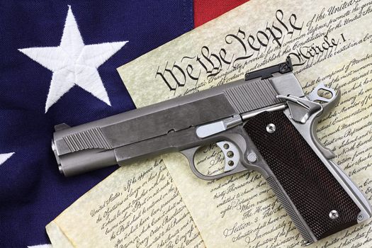 Handgun lying over a copy of the United States constitution and the American flag.

