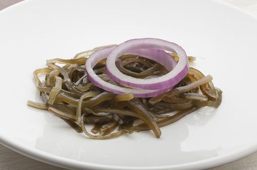 Handful of laminaria with red onion on the white plate