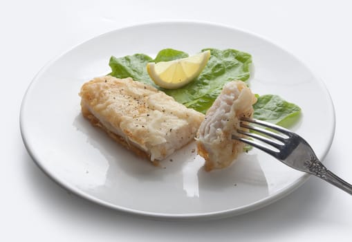 Fried fillet of pangasius with lettuce and lemon on the white plate