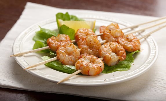 Roasted shrimps on the skewers with lettuce and lemon on the white plate