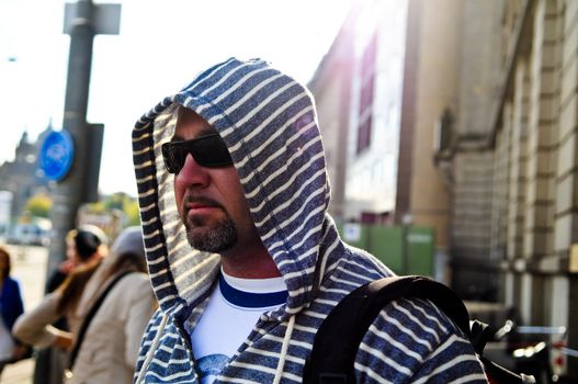 Middle age man with backpack wearing a hood traveling the city.