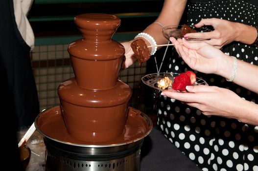 Chocolate fountain with ladies hands dipping their treats at a wedding.