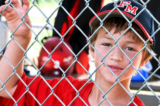 Upclose shot of a Little league baseball player standing in the dugout behind fence.