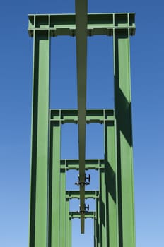 Detail of a small gantry crane painted green against the blue sky